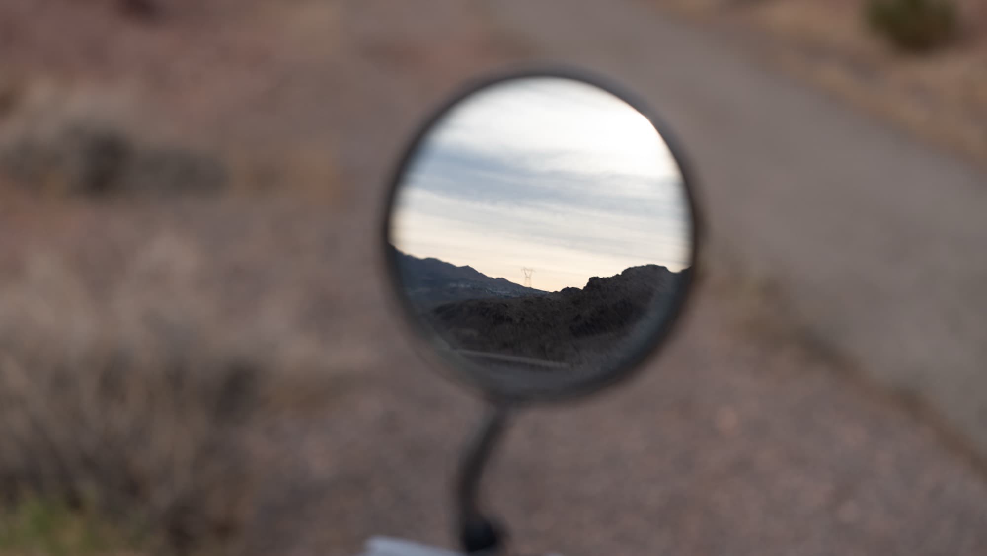 A desert road reflected in a motorcycle's round mirror