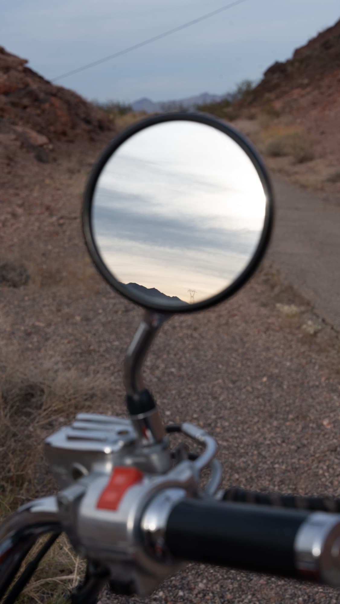 Desert sky reflected in a motorcycle's mirror on a canyon road